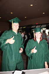 Two ɫɫ graduates in green caps and gowns.